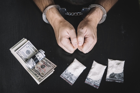 handcuffed man in front of money and illegal drugs